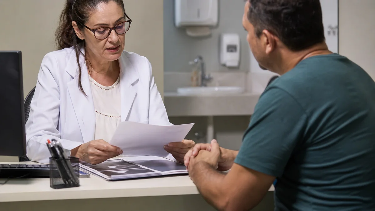 Médica analisa exames e laudo em consultório enquanto conversa com paciente trabalhador