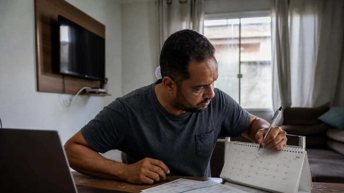 Trabalhador marca datas em calendário ao lado de documentos e carteira de trabalho sobre mesa