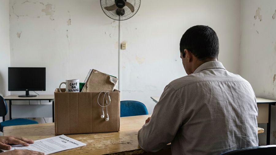 Trabalhador de escritório sentado diante de caixa com pertences e documento de rescisão sobre a mesa, pensando em seus direitos trabalhistas
