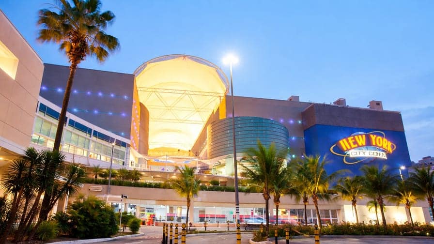 Entrada iluminada do shopping center na Barra da Tijuca, Rio de Janeiro, área comercial com lojas e circulação de trabalhadores